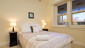A neatly made bed with a striped bedspread, two bedside lamps, a small rug, and a window with a view of a lighthouse. - Classic on George- clean, comfortable and pet friendly! - Classic heritage home with four bedrooms (Albury)