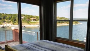 Ein Schlafzimmer mit großem Fenster mit Blick auf ein Gewässer und eine entfernte Küste.