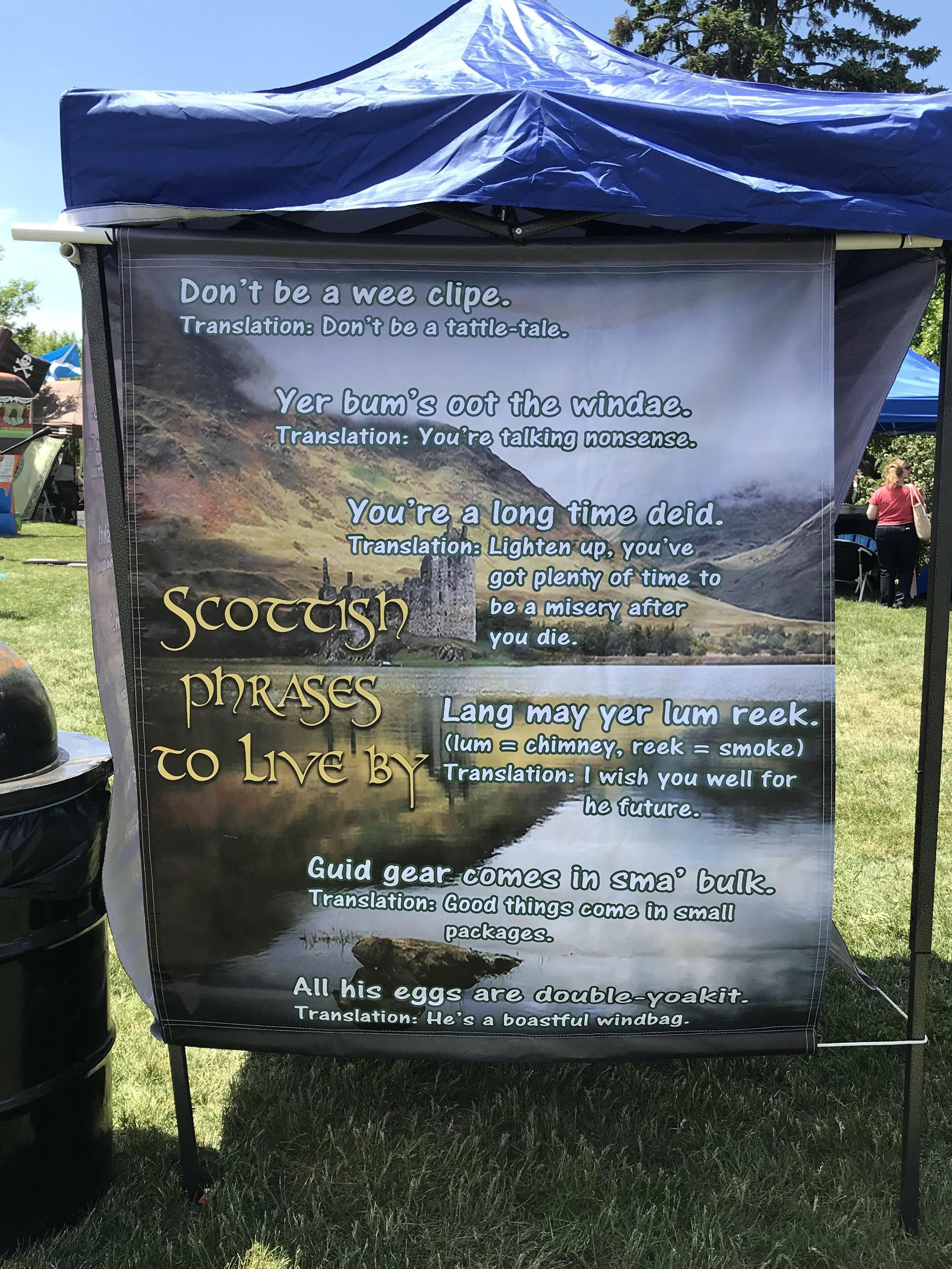 A sign with Scottish phrases and their English translations, displayed under a blue tent.