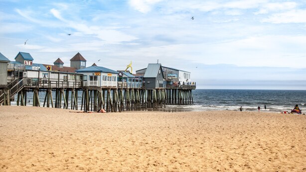 Een pier met gebouwen die zich uitstrekt over het strand, een zandstrand en de oceaan op de achtergrond.