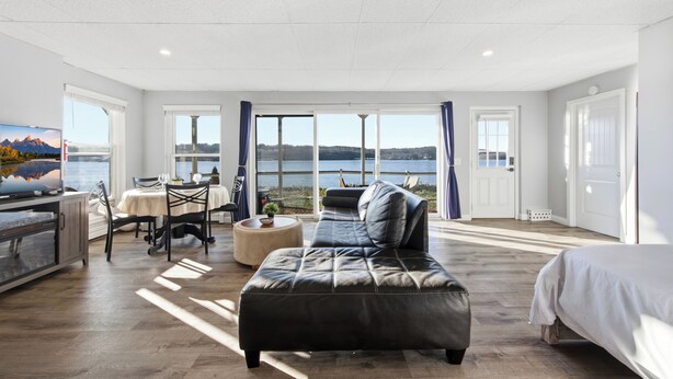 A spacious room with a large window offering a view of the water, a sofa, a dining table with chairs, and a bed.