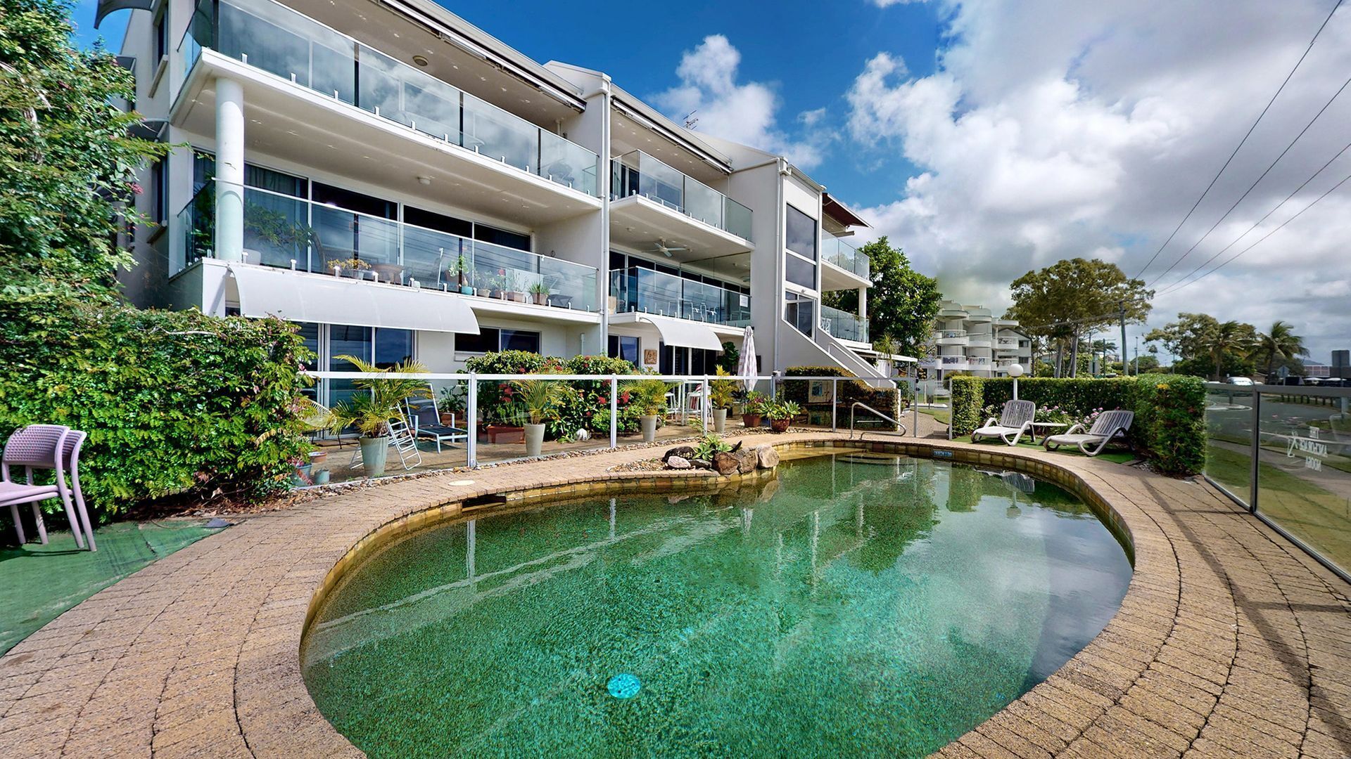 Un hotel moderno con piscina, mobiliario exterior y un jardín bien cuidado.