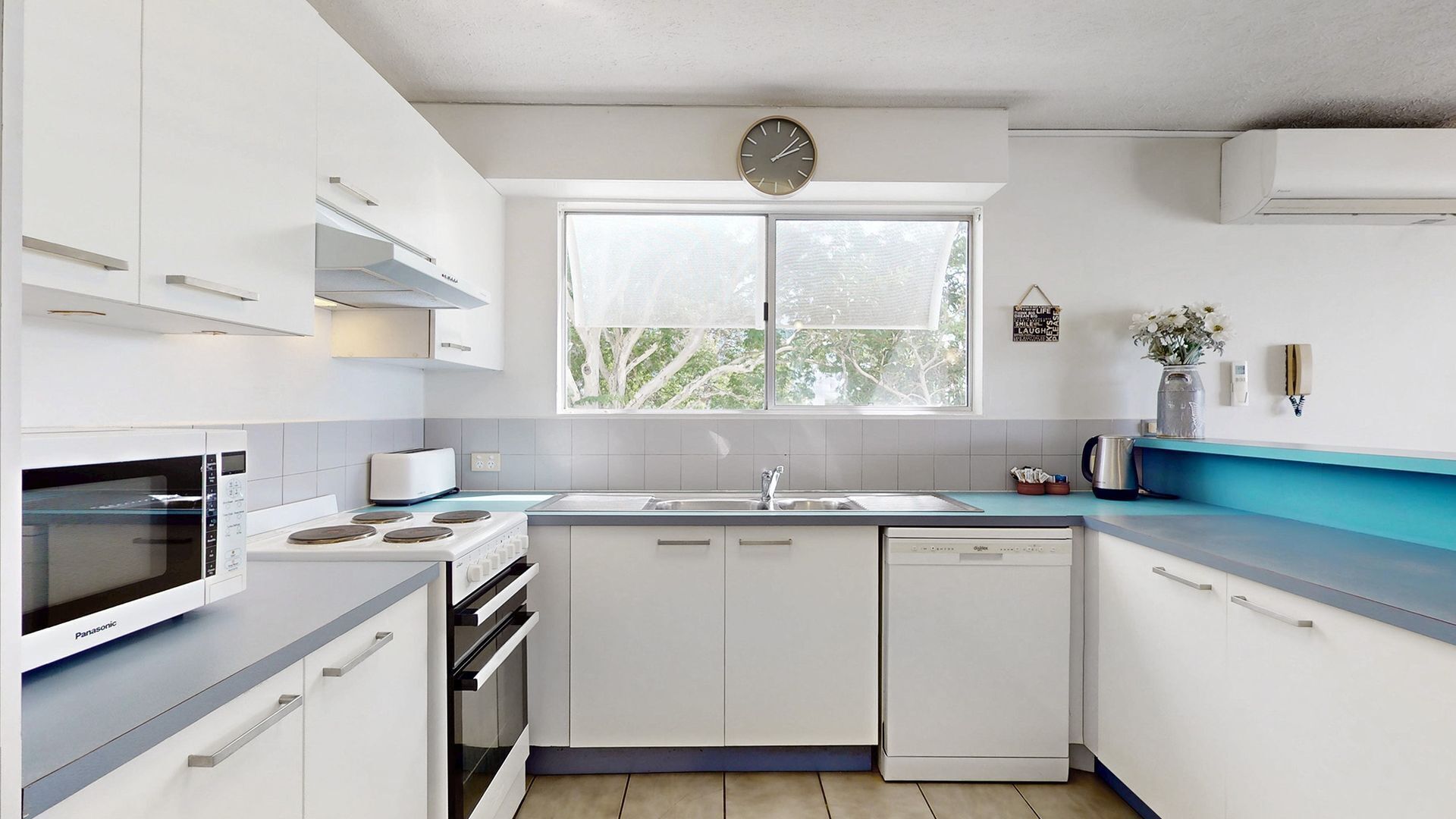 A modern kitchen with white cabinets, a built-in oven, a dishwasher, and a window with a view of trees.