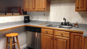 A kitchen with wooden cabinets, a stainless steel dishwasher, a sink, and a bar stool. - Farm cottage for football/graduation weekends. (Pennsylvania Furnace)