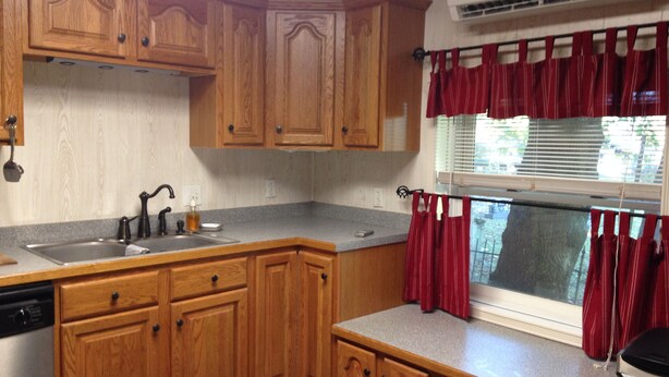 A kitchen with wooden cabinets, a stainless steel sink, a dishwasher, and a window with red curtains. - Farm cottage for football/graduation weekends. (Pennsylvania Furnace)