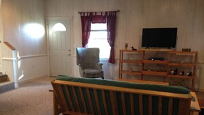 A living room with a wooden sofa, a chair, a TV stand, and a window with curtains. - Farm cottage for football/graduation weekends. (Pennsylvania Furnace)