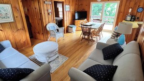 Ein gemütliches Wohnzimmer mit Holzvertäfelung, eine Essecke mit Tisch und Stühlen sowie ein Fernseher auf einem Schrank.