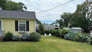 Ein Wohnhaus mit gepflegtem Rasen, einer Veranda mit Bank und verschiedenen Sträuchern und Blumen.