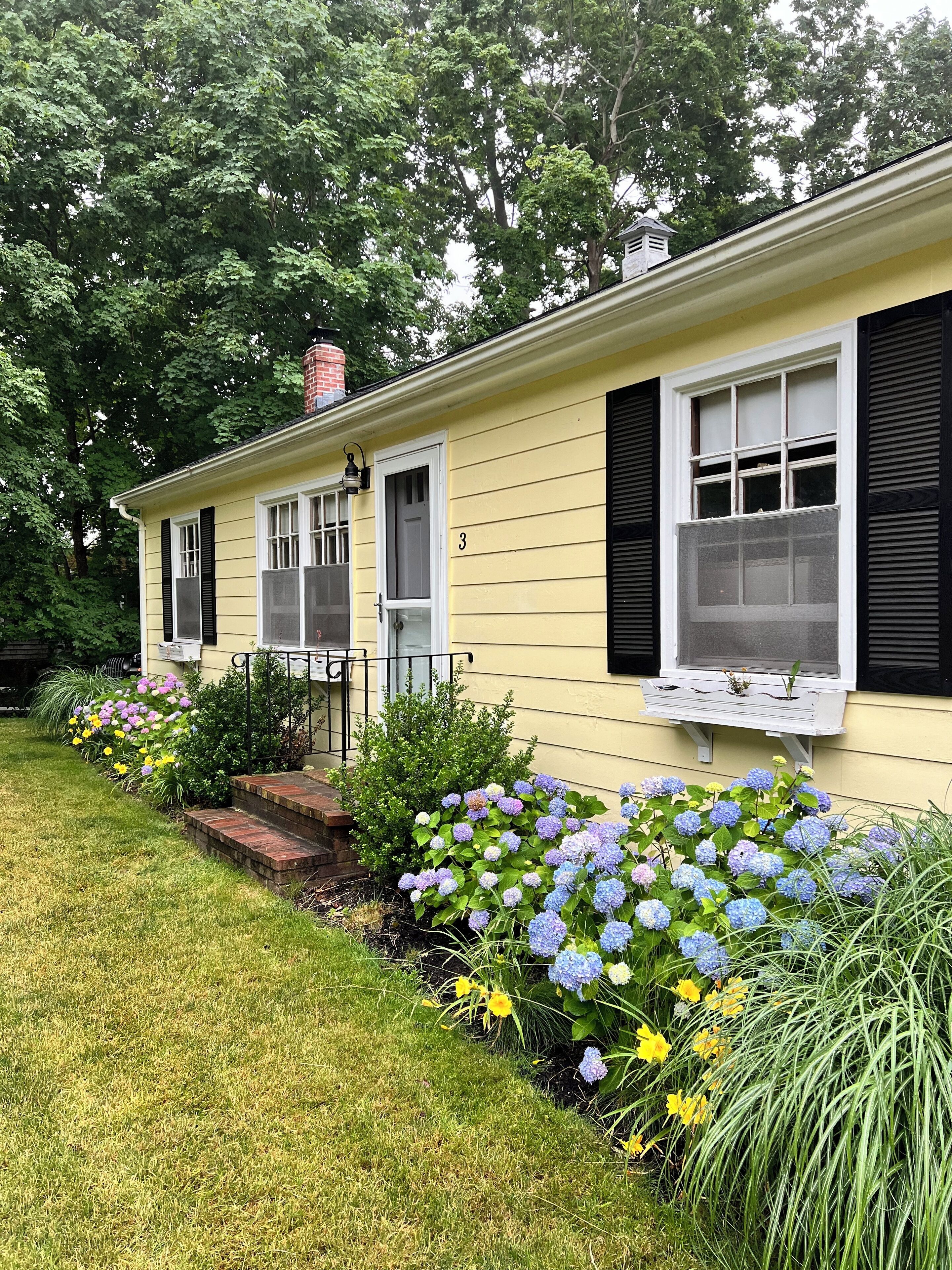 A yellow house with black shutters, a number '3' on the door, and a small porch with steps.