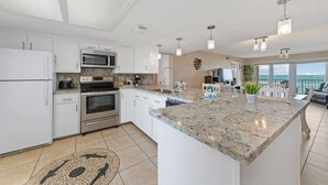 A modern kitchen with white cabinets, granite countertops, stainless steel appliances, and pendant lighting. - SPI Beach House Gateaway 1-504 (South Padre Island)