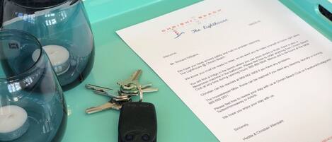A teal tray with three glass candle holders, a set of keys, and a welcome letter from a hotel.