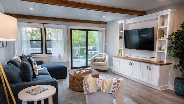 A modern living room with a sofa, ottoman, and armchair, a TV, and a large window. - Salty but Sweet - 3 min walk to Beach - Newly Renovated - Video! (Wells)