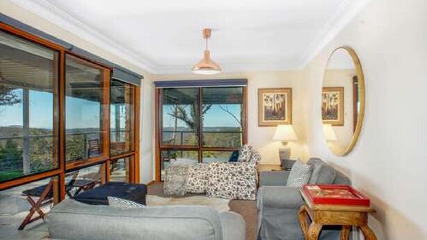 A living room with a sofa, armchairs, a coffee table, and a large mirror. There are two windows with a view of the outdoors. - Hat Hill Hideaway Amazing Valley Views (BLACKHEATH)