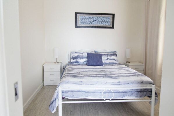 A bedroom with a bed, two bedside tables, a nightstand, and a framed artwork on the wall. - **Blue Point Cottage No 1 Bermagui** (Bermagui)