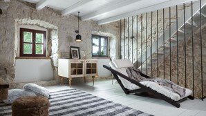 Ein Zimmer mit Steinwänden, Holzbalkendecke, einem Liegestuhl, einem Schrank und einer Treppe.