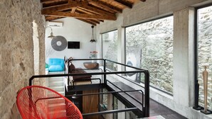 Ein modernes Interieur mit freiliegenden Holzbalken, einer Steinwand, einem großen Fenster mit Blick und einem roten Sessel sowie einem blauen Sofa.