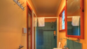 Un couloir étroit mène à une salle de bain équipée d’un lavabo, d’un miroir et d’une douche.