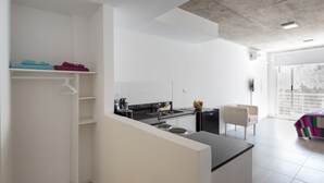 A modern kitchen with white cabinetry, a black countertop, and a small island. There is a chair and a table with a colorful tablecloth in the adjacent dining area.