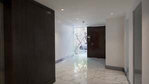 A hallway with a marble floor, dark wooden doors, and recessed ceiling lights.
