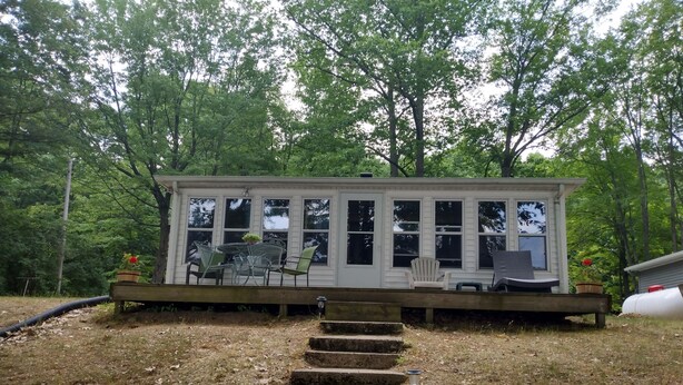 A covered outdoor seating area with a table and chairs, surrounded by trees. - Quiet Cottage On The Lake (delton)