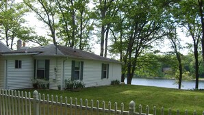 A white house with a fenced yard and a lake in the background. - Quiet Cottage On The Lake (delton)