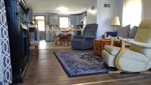 A living room with a blue armchair, a sofa, and a wooden coffee table. There is a dining area with a table and chairs in the background. - Quiet Cottage On The Lake (delton)