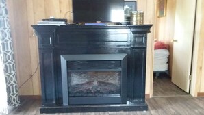 A fireplace with a television above it, a patterned rug in front, and a door leading to another room. - Quiet Cottage On The Lake (delton)