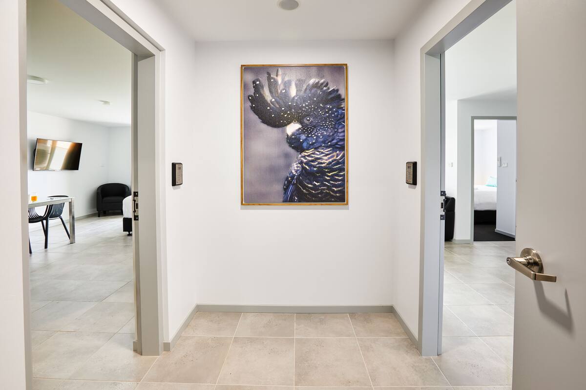 A hallway with a framed artwork of a bird, a door with a handle, and a tiled floor.
