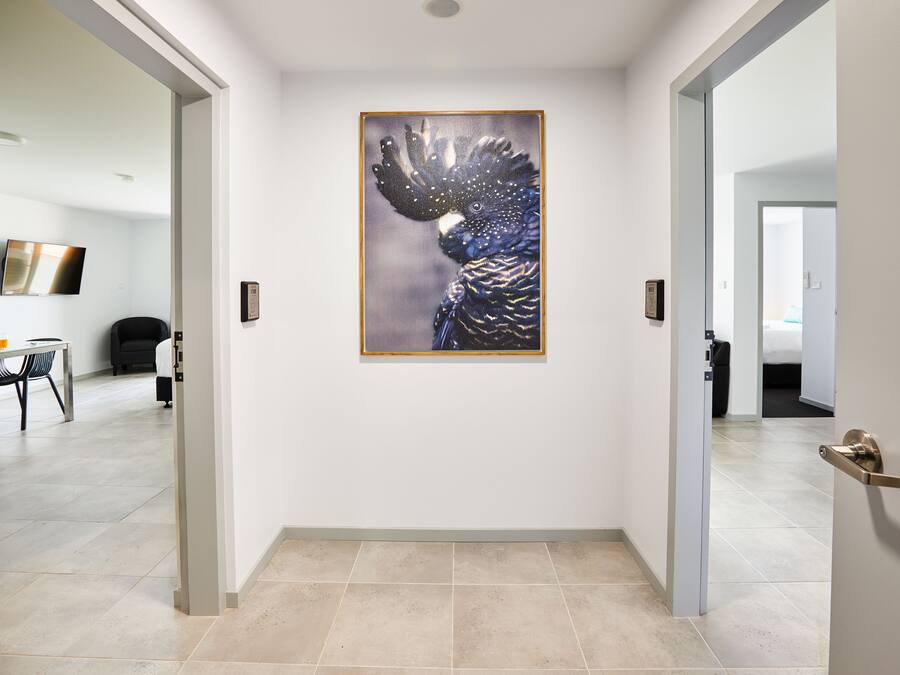 A hallway with a framed artwork of a bird, a door with a handle, and a tiled floor.