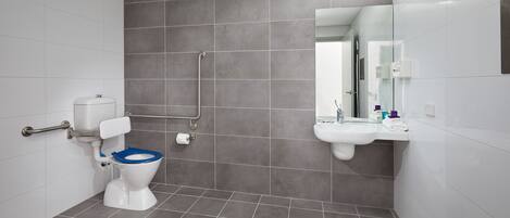 A modern bathroom with a toilet, grab bars, a sink, and a mirror.