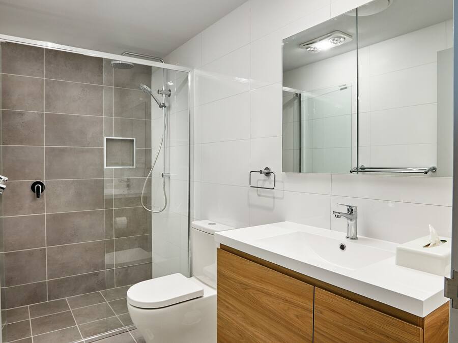 Un baño moderno con ducha de vidrio, lavamanos blanco y tocador de madera.
