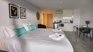 A hotel room with a large bed, a kitchenette, and a dining area. - East Maitland Executive Apartments (East Maitland)