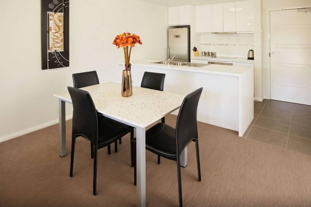 A dining area with a white table, black chairs, and a vase with orange flowers.