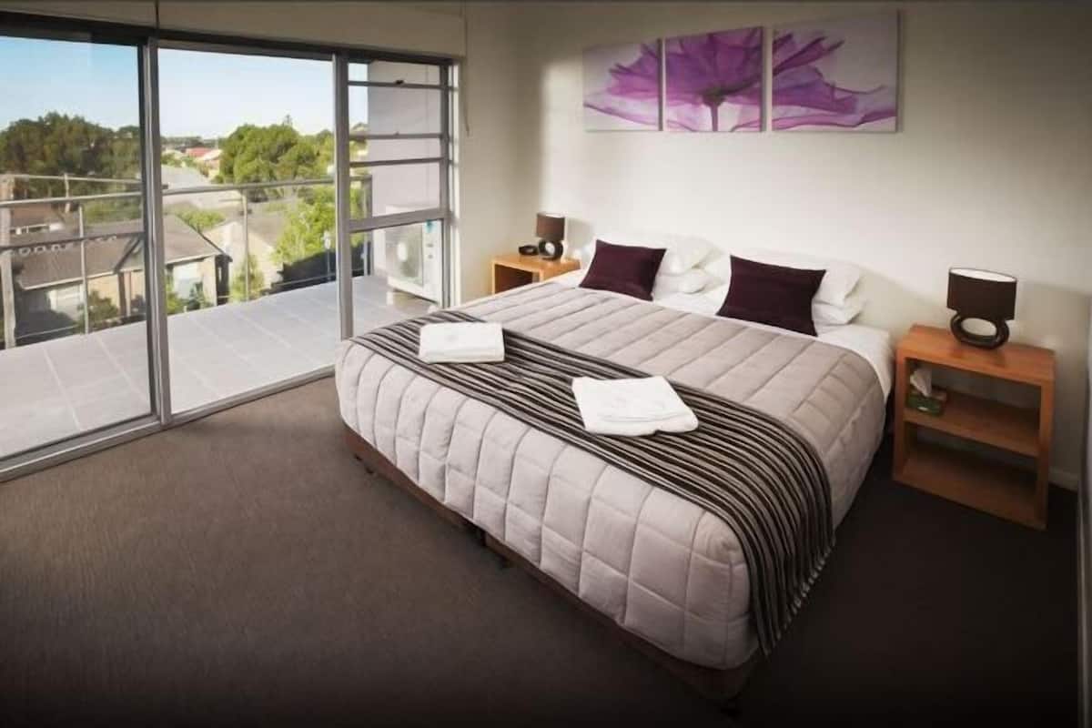 A hotel room with a large bed, a balcony, a view of the city, and a painting on the wall.
