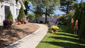 Un jardín residencial con un sendero, plantas en macetas y mobiliario exterior.