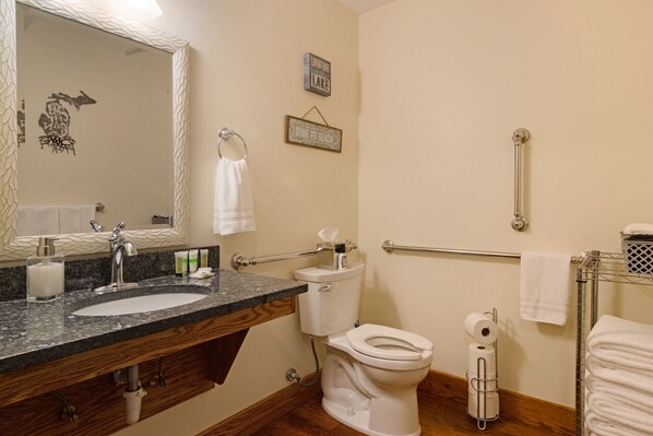 Une salle de bain avec un lavabo surmonté d’un plan de travail en granit, des toilettes blanches, un porte-serviettes et un miroir avec un cadre décoratif.