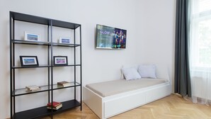 A modern room with a white bed, a black bookshelf with framed pictures, and a TV displaying a show. - Black and White , Wifi and Parking free (Praha 3)