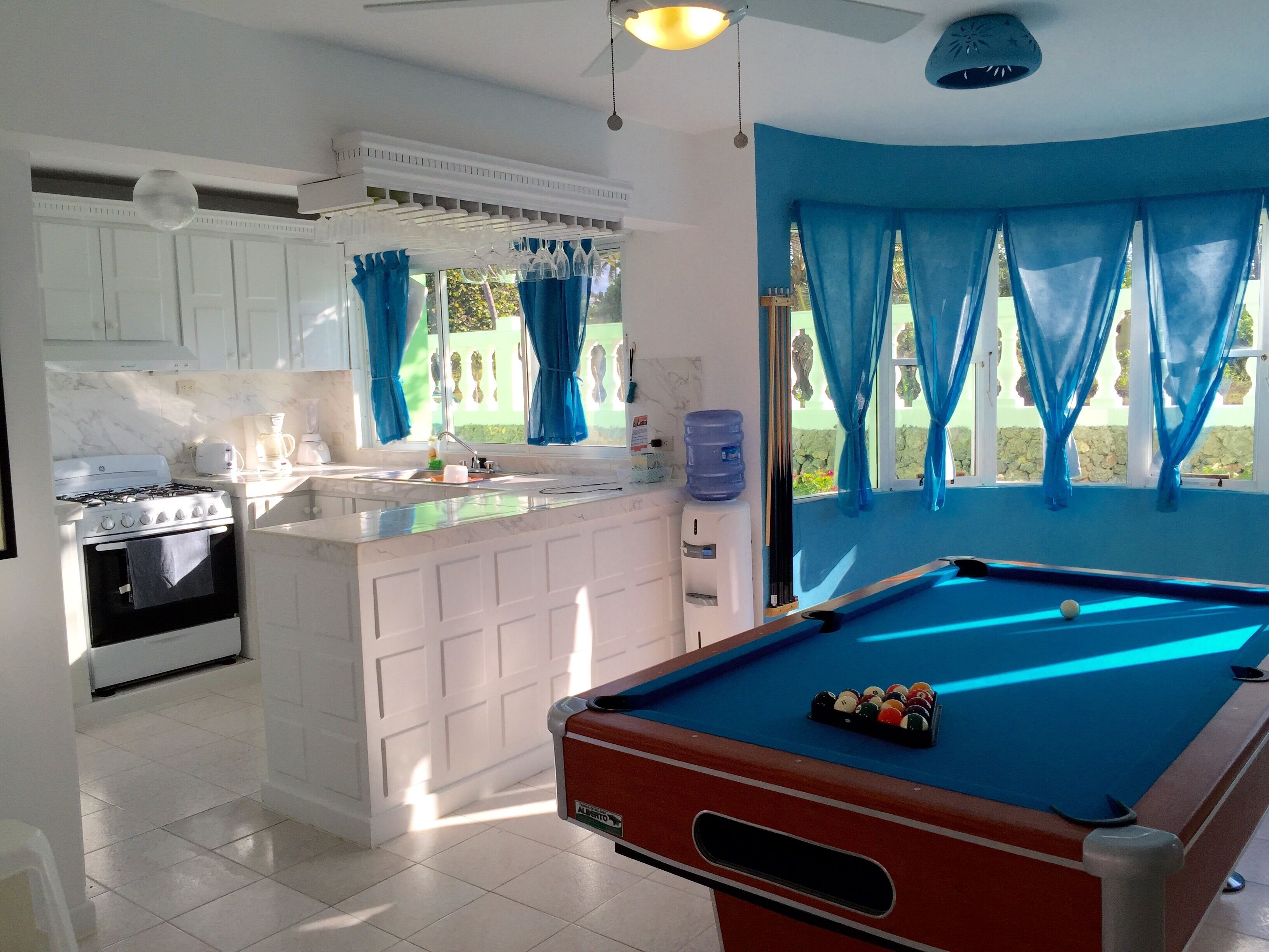 A kitchen with a built-in stove, sink, and a pool table.
