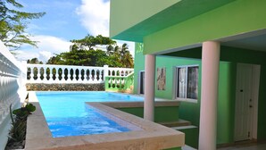Une piscine entourée d’une clôture blanche, avec des murs verts et une porte.