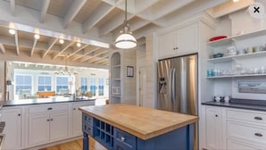 A modern kitchen with white cabinetry, a wooden island, and a stainless steel refrigerator. - Beachfront Property on Private Moody Beach (Wells)