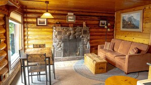 A log cabin interior with a stone fireplace, wooden furniture, and a painting on the wall.