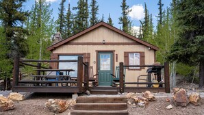A rustic cabin with a wooden deck, a green door, and a welcome sign.