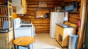 A compact kitchen with wooden walls, a refrigerator, a microwave, a sink, and a small table.