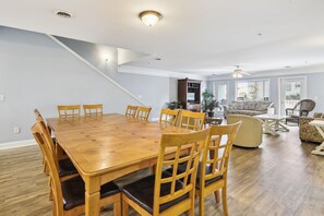 Un comedor amplio con una mesa y sillas de madera, una escalera y una sala de estar con sofá y sillones.