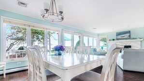 Un comedor con mesa y sillas blancas, ventanas amplias y vistas al exterior.