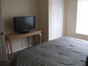 Een slaapkamer met een bed, een televisie op een houten standaard, een deur en een raam.