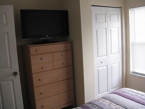 A bedroom with a TV on a dresser, a bed with a patterned bedspread, and a white door. - Venetian Bay Townhome in Quiet Location - VB011 (Kissimmee)