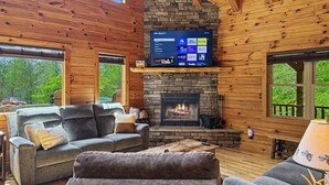Ein gemütliches Blockhaus-Interieur mit Kamin aus Stein, Holzwänden und einem flachbildfernseher darüber.