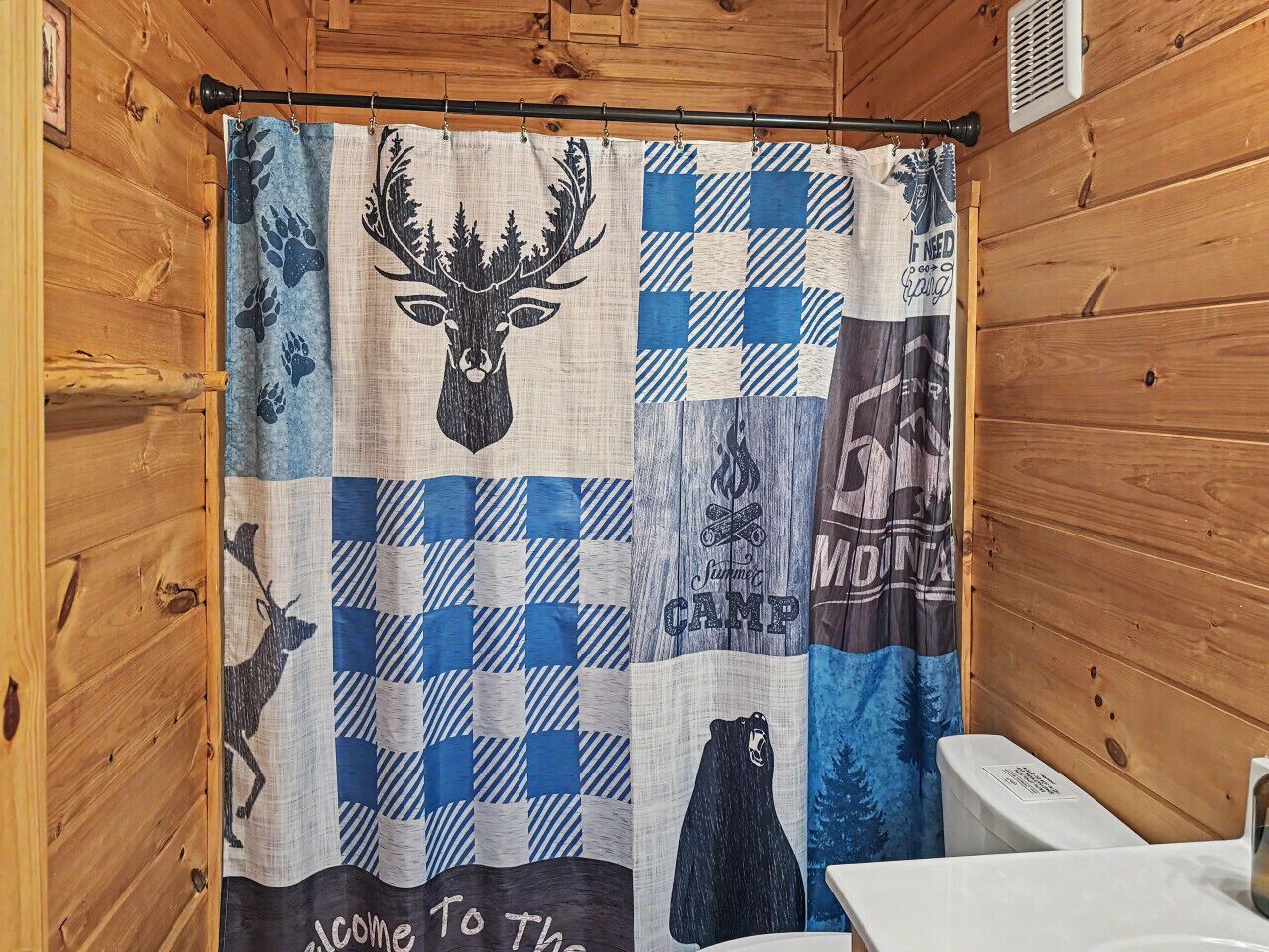 A bathroom with a wooden cabin-style interior, a shower curtain with wildlife and camp-themed designs, and a white toilet.