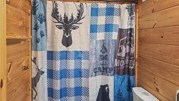 A bathroom with a wooden cabin-style interior, a shower curtain with wildlife and camp-themed designs, and a white toilet.
